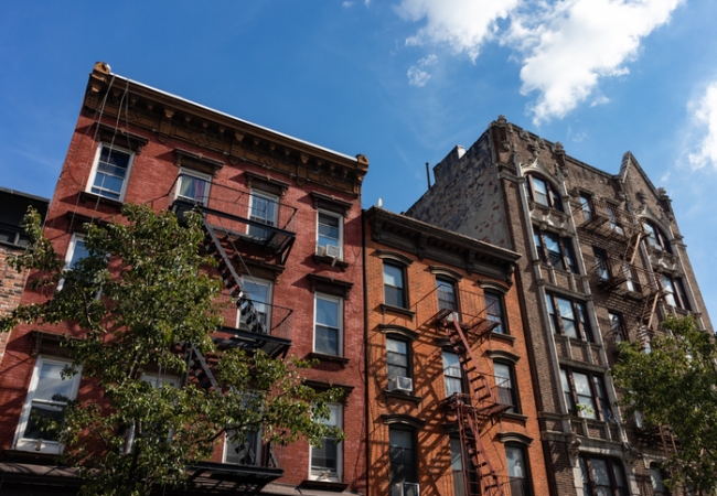 Looking up at a row of colorful old brick apartment buildings with fire escapes along a street in Williamsburg Brooklyn of New York City